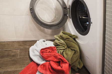 Washing machine with multicolored dirty towels on the floor near it. laundry washer with opened door. Side view. Close upの写真素材