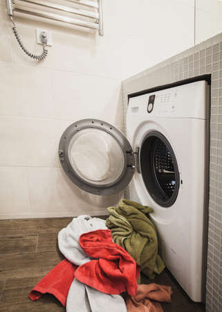 Washing machine with multicolored dirty towels on the floor near it. laundry washer with opened door. Side view. Verticalの写真素材
