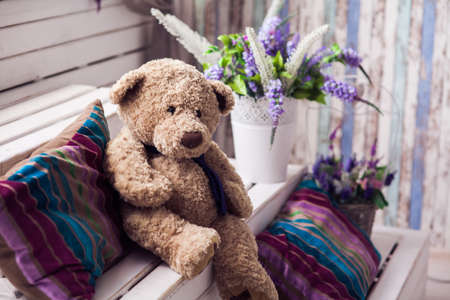 Plush Teddy bear sits among striped pillows on white wooden stairs. Spring lavender flowers in basket at the background.の写真素材