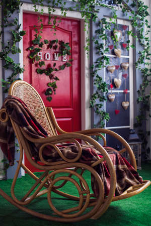 Wicker rocking chair at the spring patio with green grace lawn and red door. Close-upの写真素材