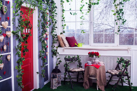 table served for tea drinking and two chairs near of red door entwined by green ivy.の写真素材