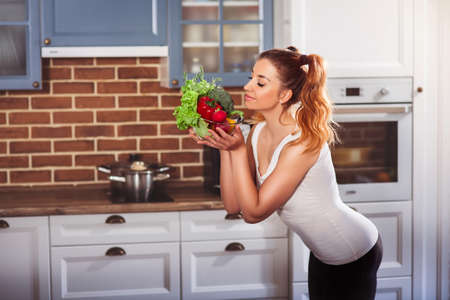 Funny athletic woman sniffing fresh vegetables in glass bowl and smiling. Light salad. Horizontalの写真素材