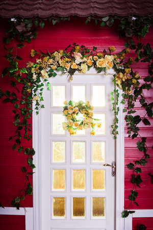 Red-painted american style wooden house. White luminous door, entwined with green ivy  and flowersの写真素材