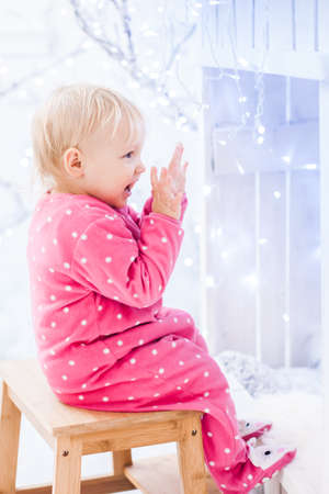 smiling caucasian baby girl dressed in pajamas sits on a chair and rejoicesの写真素材
