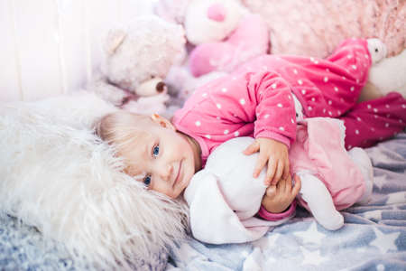 smiling caucasian baby girl lying on a fur pillow and embracing a plush bunnyの写真素材