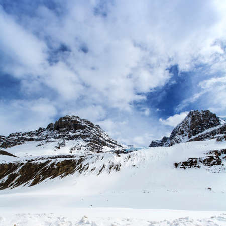 winter snow capped mountains with blue sky and white cloudsの写真素材