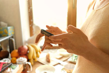 Womens hands gently hold mobile phone and type text. Bananas, tangerines, apples and other fruits in...
