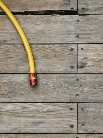 Yellow watering hose lies on wooden floor of terrace. Copy spaceの写真素材