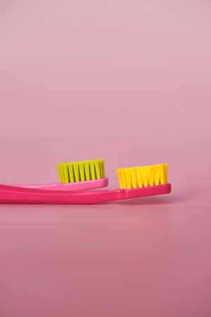 Two pink toothbrushes stand in pink glass on pink background. One brush is new and other has been used. Yellow bristles are disheveled, green bristles are new.の写真素材