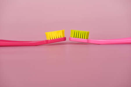 Two pink toothbrushes stand in pink glass on pink background. One brush is new and other has been used. Yellow bristles are disheveled, green bristles are new.の写真素材