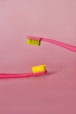 Two pink toothbrushes stand in pink glass on pink background. One brush is new and other has been...