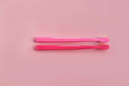 Two pink toothbrushes stand in pink glass on pink background. One brush is new and other has been used. Yellow bristles are disheveled, green bristles are new.の写真素材