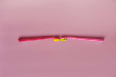 Two pink toothbrushes stand in pink glass on pink background. One brush is new and other has been used. Yellow bristles are disheveled, green bristles are new.の写真素材