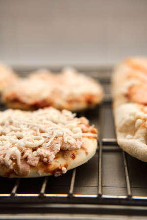 Small frozen pizza semi-finished product with tomato sause and cheese on grill prepared for baking....