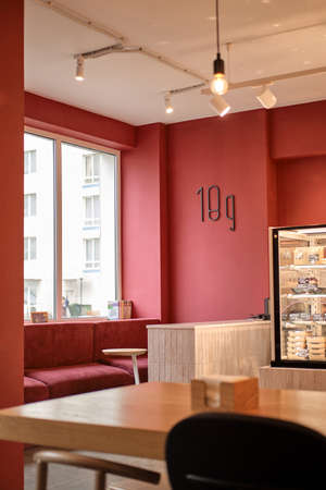 Modern cafe with red walls and red couch. Books on windowsill. Window shows multi-storey residential...