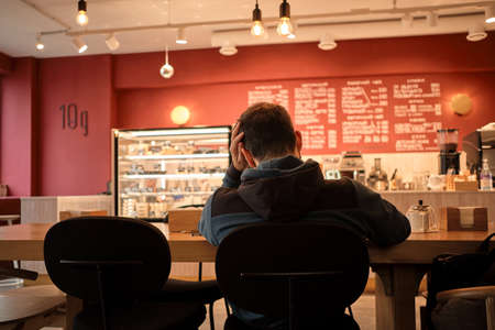 Worried busy man is sitting in cafe and working on complex project. Concept of ideas of lightbulbs over head. The chair is not comfortable, problems at work.の写真素材