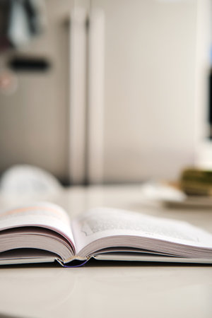 Open hardcover book with white pages lies on artificial stone table at kitchen, fridge on background. Books spine. Selective focus. Vertical stories background.の写真素材
