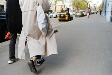 Two friends are walking down street in cool weather, raincoat fluttering in wind. One person has eco...