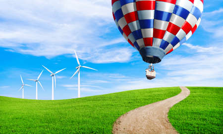 Air balloons flying in blue sky above green grass. Wind turbine in green hill. Ecology environmental concept. Beautiful summer landscape wallpaper. Spring background.の写真素材