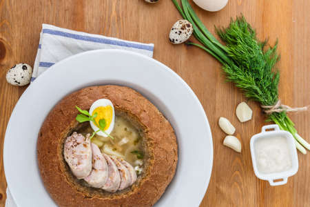 Traditional polish white borscht with eggs and sausage in bread for easter