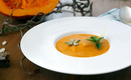A bowl of homemade creamy pumpkin soup on a rustic table with autumn decorationsの写真素材