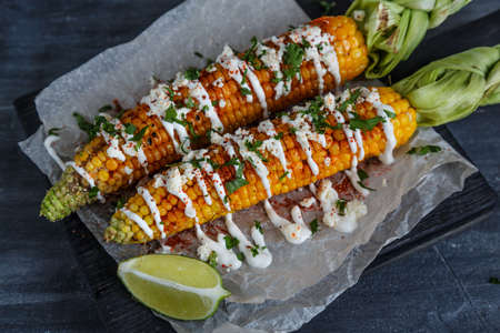 Elote or Mexican grilled corn on the cob served with cotija cheese and chili powderの写真素材