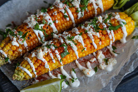 Grilled corn cobs on wooden plate, mexican style, close view.
