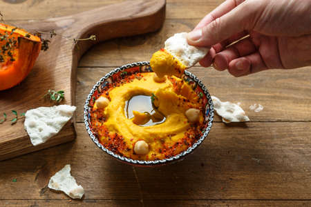 Man dip bread into pumpkin hummus on a dark wood background. the toning. selective focus.の写真素材