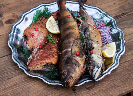 smoked fish with lemon and berries on metal plate, wooden background.