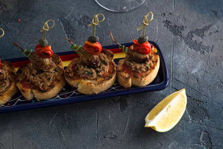 Spanish tapas. Montaditos. Bread slices with tuna, peppers and capers. Typical appetizer. Dark photo