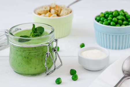 cream of green peas soup with mint in jars on a white wooden background.の写真素材