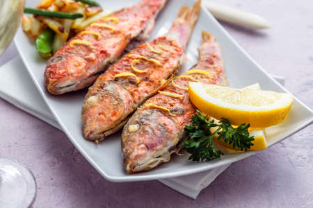 Plate of fried small fish red mullet and lemon, close view.
