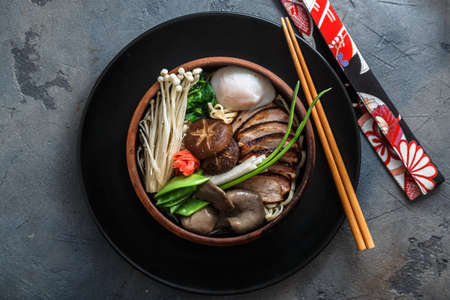 Ramen noodles with duck, egg, enoki and shiitake mushrooms with broth on dark background
