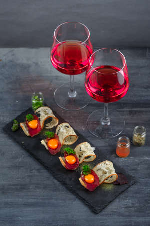 Appetizers - cured meat, crusty bread, yolk and cheese - on stone board with two glasses of wineの写真素材