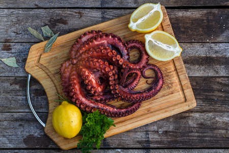 Boiled octopus ready for serve with lemon and parsley on wooden boardの写真素材