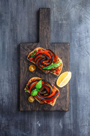 Appetizers with grilled aubergines, bell peppers and basil. Dark background.