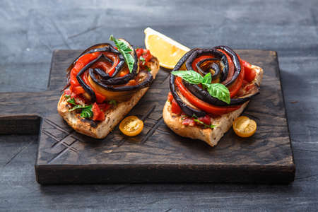 Two bruschettas with baked aubergines and peppers on black background.の写真素材