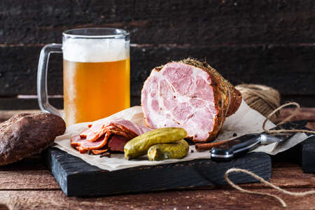 Delicious smoked ham on a blackwooden board with beer and picklesの写真素材