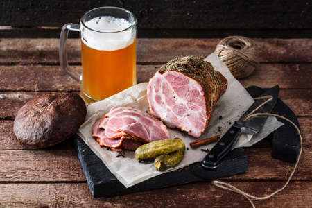 Delicious smoked ham on a blackwooden board with beer and picklesの写真素材