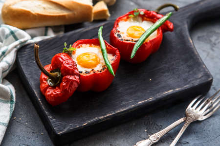 Egg baked in red bell pepper with sausage and tomato on a black board, close view.
