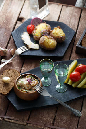 Pickled tomatoes, cucumbers, mushrooms and onion on wooden background with fork and shots of vodka