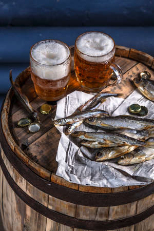 Beer mugs with dried fishes on a wooden barrel, dark photoの写真素材