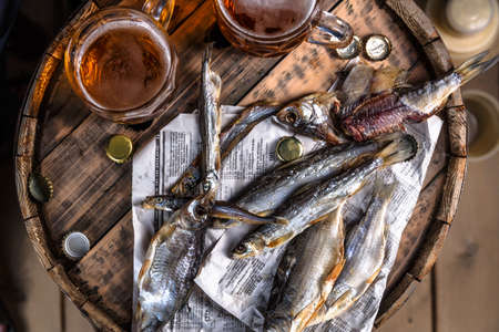 Beer mugs with dried fishes on a wooden barrel, dark photoの写真素材