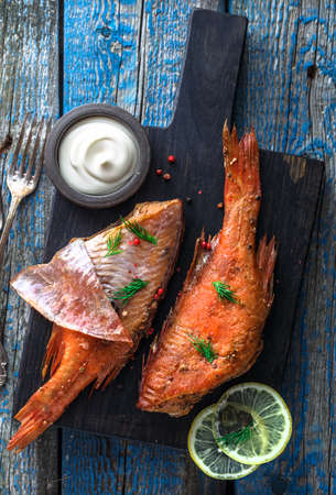 Delicious smoked fish ocean perch on wooden background, top view