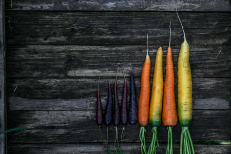 Colored organic carrots over rustic wooden background closeup. Top view