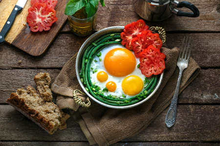 Sunny side fried eggs in a copper pan with tomatoes and green beans, copy space.
