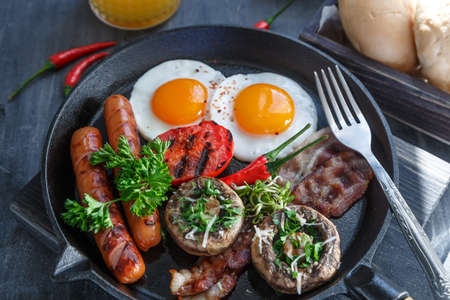 Close view of English Breakfast in a pan with fried eggs, sausages, bacon, mushrooms, jam and orange juice on dark stone background.の写真素材