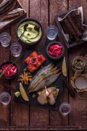Assorted marinated fish on dark cutting board with vodka shots.