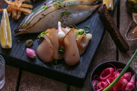 Assorted marinated fish on dark cutting board with vodka shots.