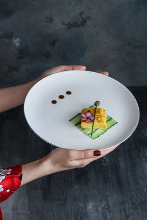 Woman hands hold a plate with tamagoyaki, copy space